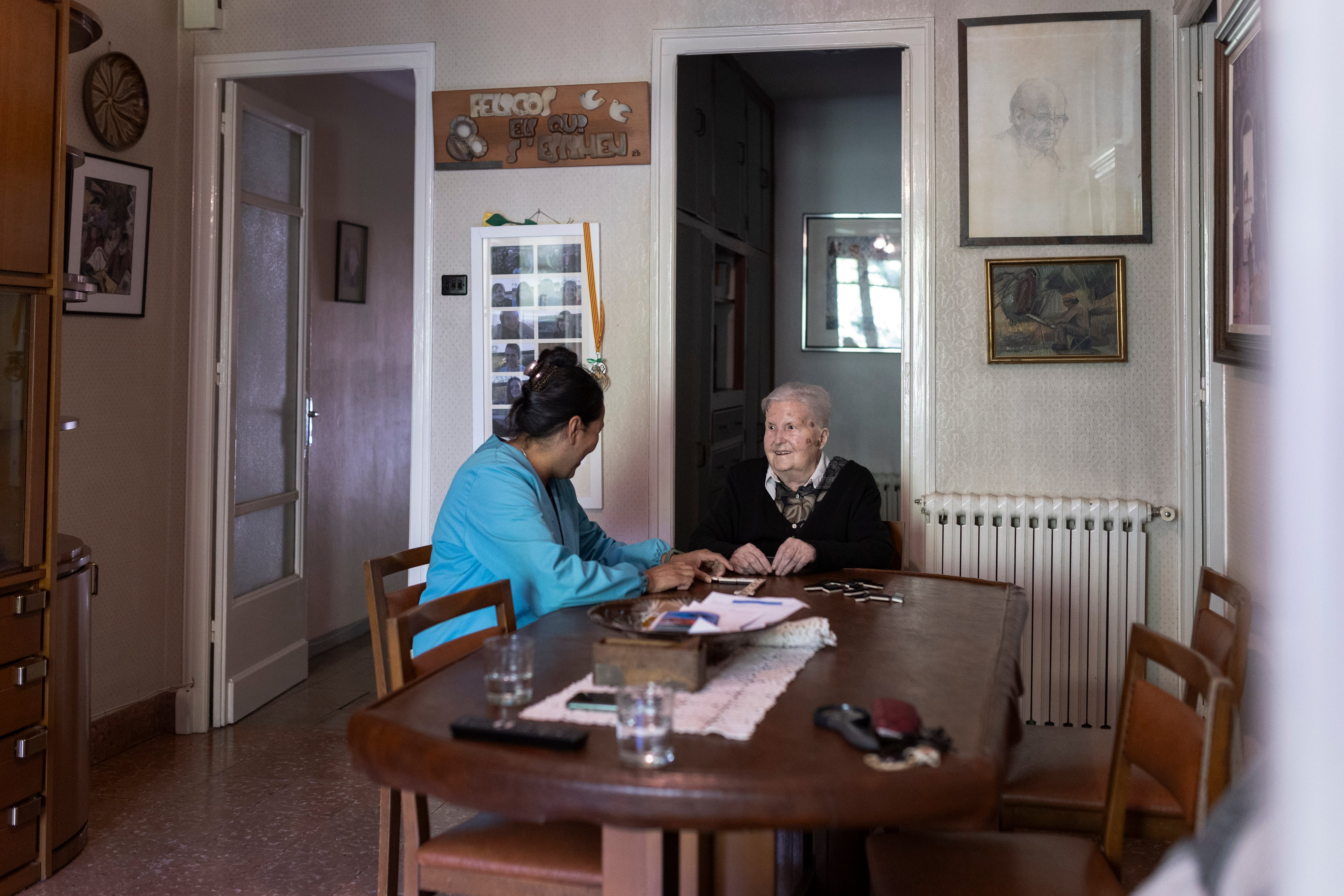Rosa Prat juega con Marisol, trabajadora de ayuda a domicilio, al dominó, en su casa, en Manresa. 