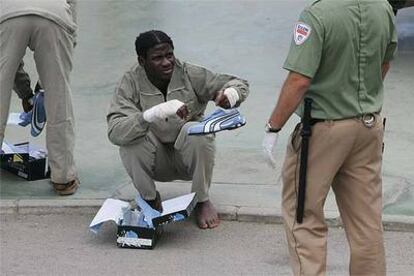 Un inmigrante herido que entró ayer en Ceuta pide ayuda a un guarda jurado para ponerse las zapatillas.