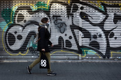 Una mujer camina por una de las aceras laterales de Rambla de Badal mientras pasa por delante de una persiana pintada con un graffiti.