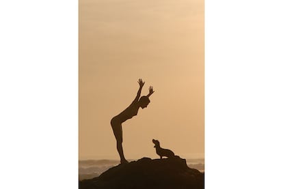 Una mujer desnuda juega con su perro junto al mar.