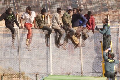 Dos guardias civiles subidos a una escalera hablan con algunos de los inmigrantes que se han quedado subidos a la valla del punto fronterizo de Melilla.