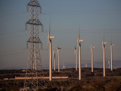 Molinos de un parque eólico junto a una torre del tendido eléctrico en Cataluña.