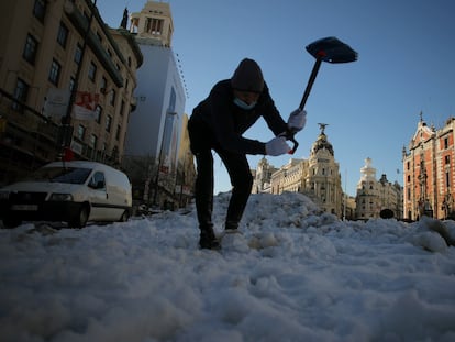 Una persona, con su coche a la izquierda averiado, intenta romper hielo con una pala, en la calle Alcala.