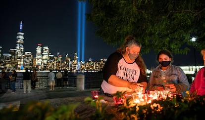Un grupo de gente enciende velas en recuerdo de las víctimas del 11-S. Al fondo, un tributo de luz instalado en el One World Trace Center por el vigésimo aniversario de los atentados.