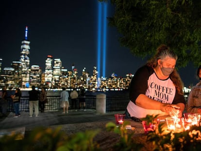 Un grupo de gente enciende velas en recuerdo de las víctimas del 11-S. Al fondo, un tributo de luz instalado en el One World Trace Center por el vigésimo aniversario de los atentados.