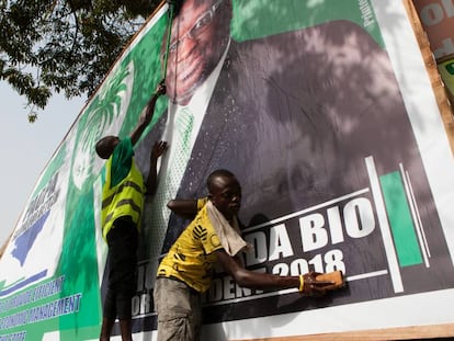 Dos chavales lavan el cartel electoral de Julius Maada Bio, candidato a la presidencia por el SLPP, en el Cotton Tree, uno de los lugares más simbólicos de la capital de Sierra Leona.