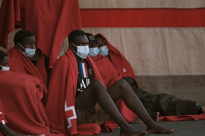 Un grupo de hombres espera con unas mantas a recibir asistencia sanitaria. Fueron rescatados por Salvamento Marítimo el 20 de marzo de 2021 y trasladados al puerto de Arguineguín (Gran Canaria) después de ser localizados en un cayuco 22 kilómetros al sur de la isla.