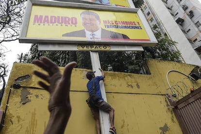 Un manifestante trepa para vandalizar un cartel propagandístico de la campaña de Nicolás Maduro.