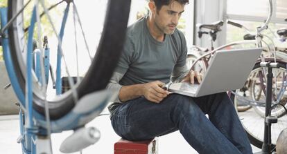 Hombre usando una computadora port&aacute;til en la tienda de bicicletas