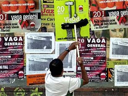 Imagen de un joven pegando carteles de la convocatoria de huelga del 20-J
