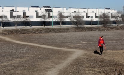 Una mujer pasea por un descampado y, asu espalda, la última urbanización de 158 nuevos chalets unifamiliares terminada en Perales del Río (Getafe).