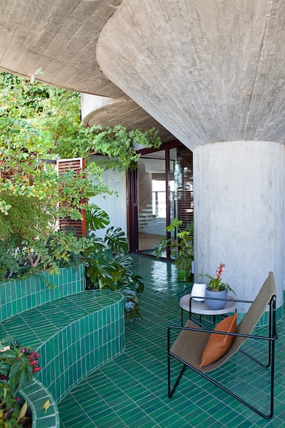 Un azulejo verde, que evoca los años sesenta, reviste tanto el suelo como el equipamiento hecho a medida de las terrazas, conformando maceteros, bancos e, incluso, la funda de la bañera. La butaca es el modelo Desert Olive de Ferm Living.