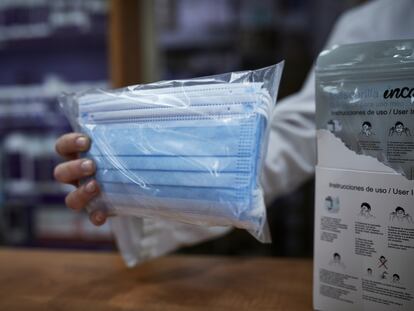 Una farmacéutica enseña a un cliente un paquete de mascarillas en una farmacia de Madrid.