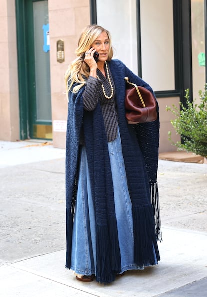 En una de las últimas escenas del rodaje el pasado otoño, Sarah Jessica Parker lleva falda larga vaquera con americana y un sobretodo de punto. Las perlas y el bolso de mano extragrande que completan el 'look' son sello de la casa.