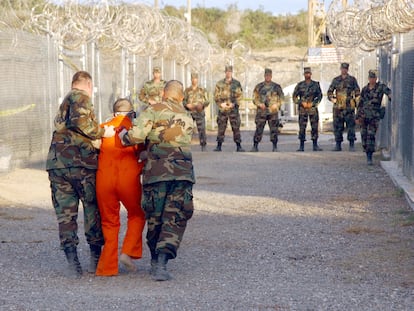 Dos militares trasladan a un detenido, vestido con un mono naranja, a su celda, en enero de 2002 en la cárcel de Guantánamo.