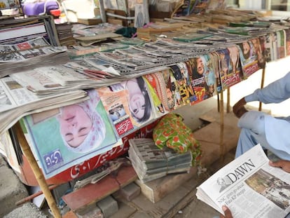 Un hombre lee un ejemplar del periódico 'Dawn' en un kiosko. 