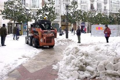 Varios ciudadanos contemplan hoy el trabajo de una máquina quitanieves en las calles del centro de Burgos.