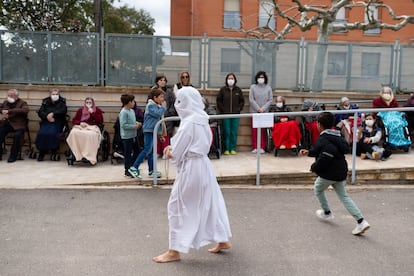 Un grupo de niños juega alrededor de un cofrade mientras los ancianos de la residencia del pueblo observan el paso de la procesión. Cada año el desfile para frente al centro de mayores para realizar un rezo junto a los residentes.