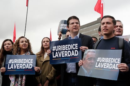 El senador Miguel Uribe (centro) junto a otros simpatizantes del expresidente colombiano sostienen carteles de apoyo este lunes, frente a los juzgados de Paloquemao en Bogotá.