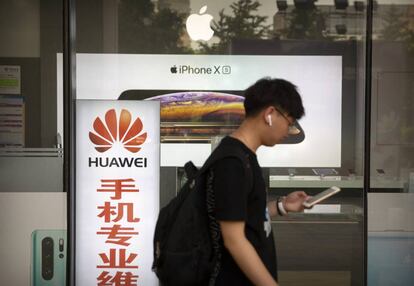 Homem caminha ao lado de uma loja com anúncios da Huawei e da Apple, em Pequim, na sexta-feira.