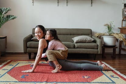 Una madre práctica yoga con su hija en el salón.