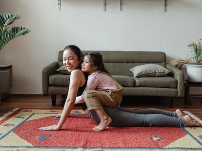 Una madre práctica yoga con su hija en el salón.