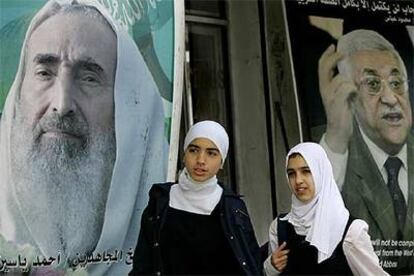 Dos muchachas caminan en Gaza junto a carteles del fundador de Hamás (izquierda) y de Mahmud Abbas.