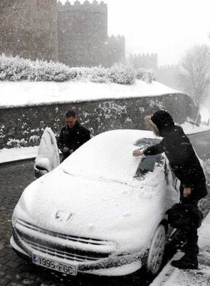 Dos personas retiran la nieve de su coche junto a la muralla de Ávila.