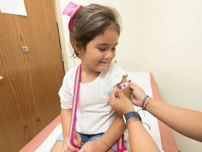 Una enfermera coloca una tirita en el brazo de una pequeña que acaba de recibir una vacuna.