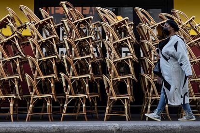 Una mujer pasa junto a las sillas apiladas de la terraza de un café, en París, Francia. El presidente francés, Emmanuel Macron, anunció que tiene intención de permitir la apertura de las terrazas de cafés, bares y restaurantes junto con museos, aunque no concretó fechas.