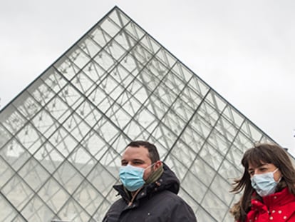 Dos personas con mascarillas pasan frente al Museo del Louvre de París.