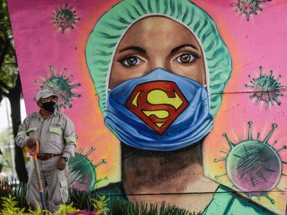 Un jardinero con mascarilla trabaja junto a un mural, en Ciudad de México.