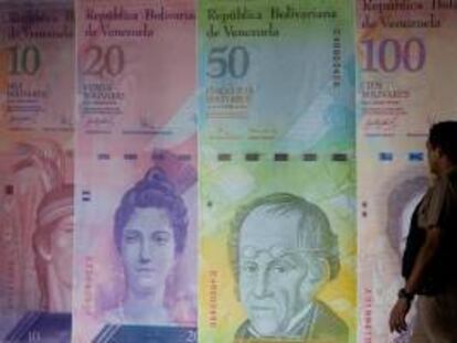 Un hombre camina frente a unos afiches de billetes venezolanos en Caracas. EFE/Archivo