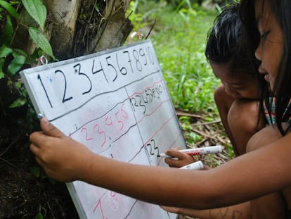 Dos niños Orang Rimba escriben números en una pizarra.