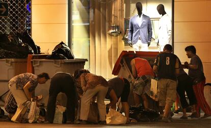 Un grupo de personas busca entre los contenedores de basura de un centro comercial de la Calle Alberto Aguilera de Madrid.