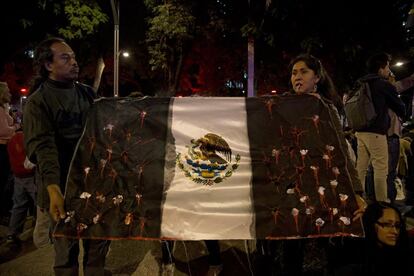 Dos personas sujetan una bandera con fotos de los desaparecidos sangrando en la marcha por el aniversario de los dos años de gestión de Peña Nieto, a la que se han sumado los manifestantes por los 43 desaparecidos para exigir justicia.