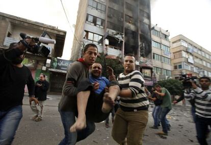 Dos hombres transportan a un herido despu&eacute;s de que la Aviaci&oacute;n israel&iacute; alcanzara el edificio que alberga los centros de prensa en Gaza.
