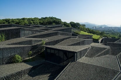 El terreno marcó, en el caso del Museo de la Academia China de Arte Popular de Hangzhou, en China, el punto de partida del proyecto que firma el japonés Kengo Kuma. El arquitecto explica que la ladera en el que se asienta el museo estaba antiguamente ocupada por una plantación de té, y que la intención era subrayar la topografía irregular del lugar: “Los pisos del edificio siguen las subidas y bajadas de la pendiente”. Esto se logró a través de un rompecabezas a base de paralelogramos conectados. “La pared exterior está cubierta con una pantalla de azulejos sostenidos por cables de acero inoxidable, así se controla el volumen de luz solar que entra en las habitaciones interiores. Las tejas antiguas utilizadas, tanto en las pantallas como en los techos, proceden de construcciones de la zona. Todo tiene tamaños diferentes, lo que ayuda que la arquitectura a fundirse con su entorno de forma natural”, se lee en la memoria del proyecto, que se finalizó en 2015.