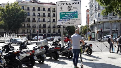 Un usuario de patinete eléctrico pasa junto a un cartel que avisa de la prohibición al paso de los vehículos más contaminantes en la capital, instalado en la glorieta de Bilbao.