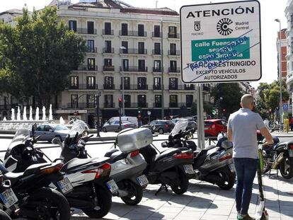 Un usuario de patinete eléctrico pasa junto a un cartel que avisa de la prohibición al paso de los vehículos más contaminantes en la capital, instalado en la glorieta de Bilbao.