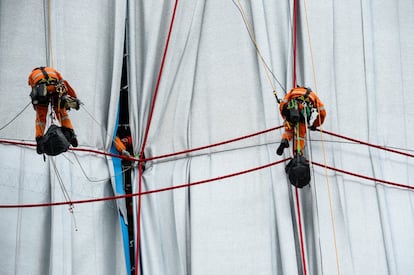 Los obreros suspendidos con arneses han asegurado la tela con cuerdas rojas, tal y como lo ideó Christo.