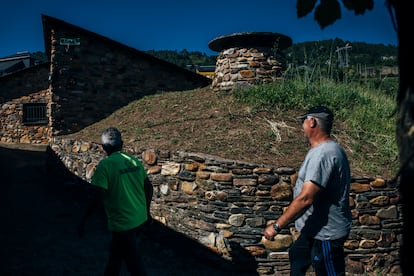 Tito Rodríguez Ferrer y Pepe Simón Rodríguez atraviesan una calle de Vilamartín de Valdeorras donde se adivina la presencia de una cueva por el montículo rematado en chimenea.