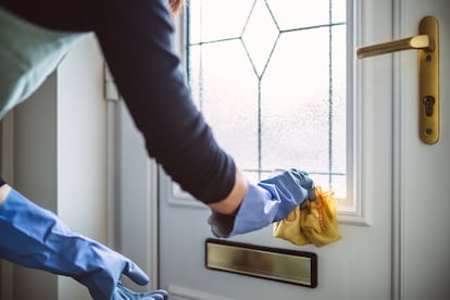 Una empleada de hogar limpia la puerta de una casa.