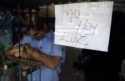 Empregado atrás da porta de uma loja fechada em Caracas, onde um cartaz avisa: “Não há luz”.