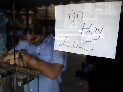 Empregado atrás da porta de uma loja fechada em Caracas, onde um cartaz avisa: “Não há luz”.