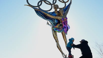 Homem brinca com criança ao lado de escultura com os anéis olímpicos no Parque de Shougang, em Pequim, nesta terça-feira.