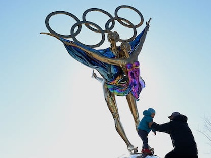 Homem brinca com criança ao lado de escultura com os anéis olímpicos no Parque de Shougang, em Pequim, nesta terça-feira.