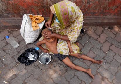 Una mujer le corta el pelo a su hijo en una calle de Kolkata (India). 