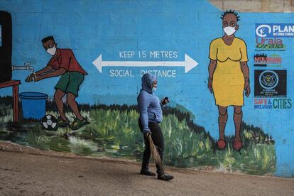 Una mujer con una máscara facial pasa junto a un graffiti que promueve el distanciamiento social, para frenar la propagación de la covid-19 en Kibera, Nairobi.