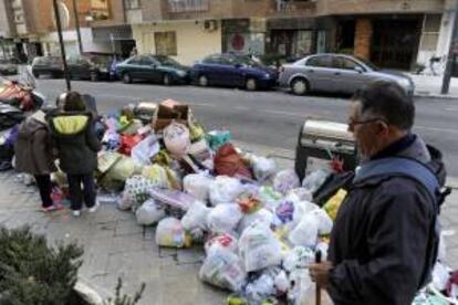 Unas personas caminan junto a bolsas de basura apiladas en la acera de una calle de Granada ayer, durante el segundo día de la huelga en la empresa Inagra, concesionaria del servicio de limpieza y recogida de basura de la capital granadina, lo que ha provocado ya la acumulación de cerca de 250 toneladas de residuos en las calles de la ciudad.